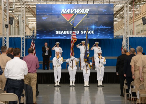 A color guard and naval officers saluting an audience from a stage